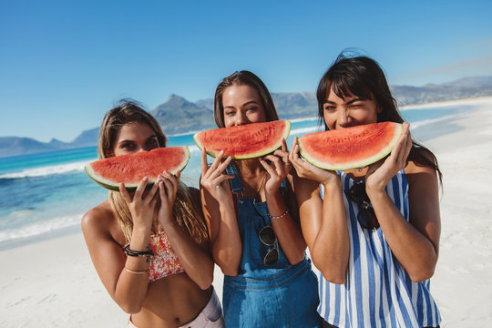 Young women having fun on the beach and eating watermelon