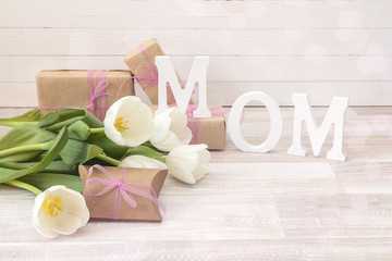 Mothers day message with white tulips and gift boxes on white wooden board.