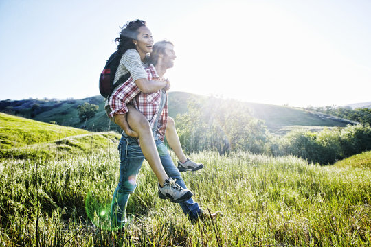 Smiling Man carrying girlfriend piggyback on hill