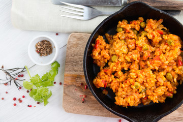Vegan paella in cast iron pan on white wooden table with cutlery, napkin,herbs and spices Top view. Corner location.
