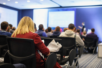 Obraz premium Business and entrepreneurship symposium. Speaker giving a talk at business meeting. Audience in the conference hall. Rear view of unrecognized participant in audience.