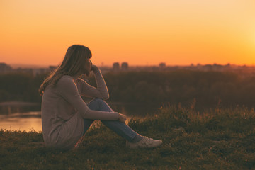 Sad woman sitting at the sunset and thinking.