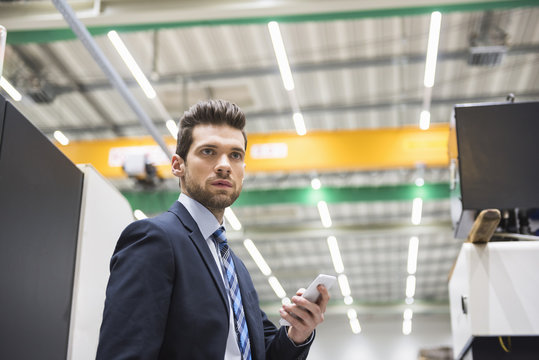Businessman in factory shop floor holding cell phone