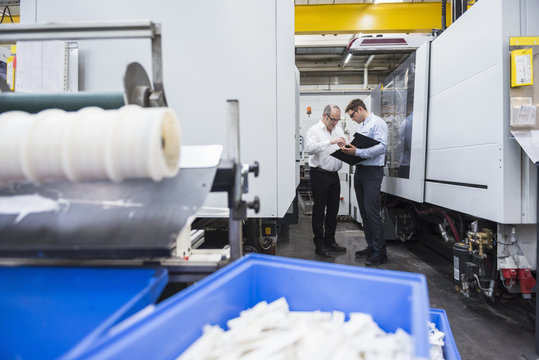 Two men talking among machines in factory shop floor
