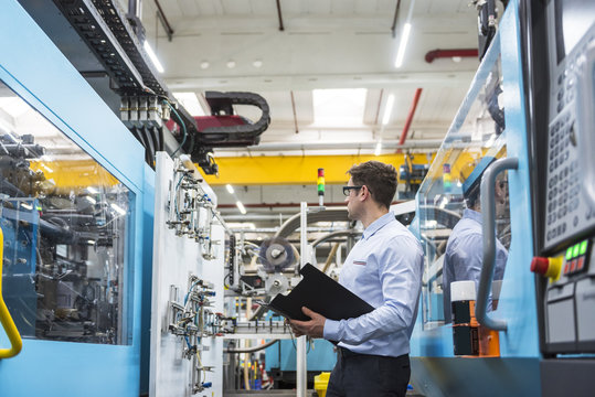 Man with documents standing among machines in factory shop floor