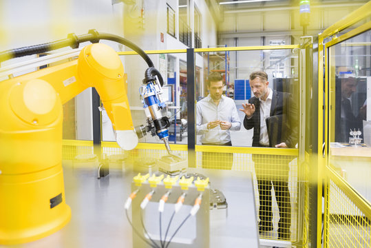 Two businessman observing industrial robots in factory