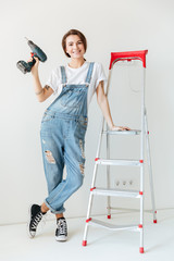 Smiling woman with drill leaning on ladder