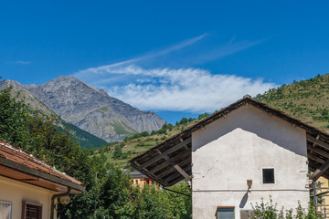 Fototapeta na wymiar Travelling in Italian Alps - Little alpine town house Highly in mountains at hot shiny summer morning with blue cloudy sky