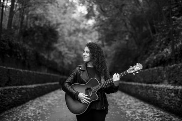 Beautiful young woman playing guitar on forest, fashion lifestyle. Girl wearing black jacket. Image...