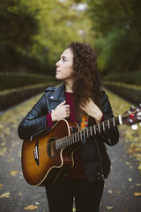 Beautiful young woman playing guitar on forest, fashion lifestyle. Girl wearing black jacket.