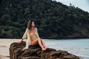 Beautiful girl in a swimsuit posing on rocks in the sea. Against the background of the sea .