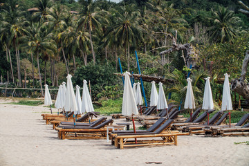 Fototapeta na wymiar Bamboo Loungers on the beach in front of the hotel, white umbrellas