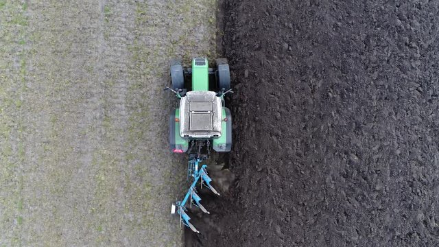 Aerial of modern tractor plowing bird view from sky perspective of farm implement used in farming for initial cultivation of soil in preparation for sowing seed and planting to loosen turn soil 4k