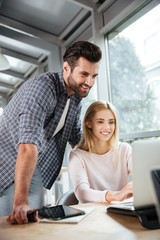 Smiling two colleagues in office coworking while using laptop