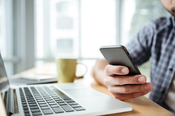 Cropped image of young man using laptop computer and phone.