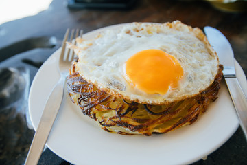 Potato pancakes with fried eggs are served with a knife and fork. On the oak table. Cafe by the sea.