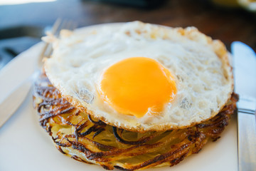 Potato pancakes with fried eggs are served with a knife and fork. On the oak table. Cafe by the sea.