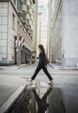 Reflection in puddle of Chinese businesswoman crossing street