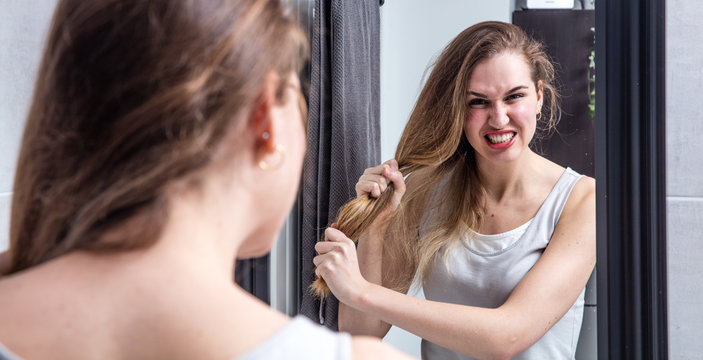 angry young woman pulling out her long dry tangled hair