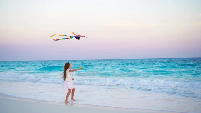 Adorable little girl with flying kite on tropical beach. Kid play on ocean shore with beautiful sunset