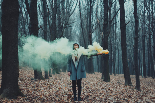 Woman holds up yellow and green smoke flare to signal for help in the middle of nature