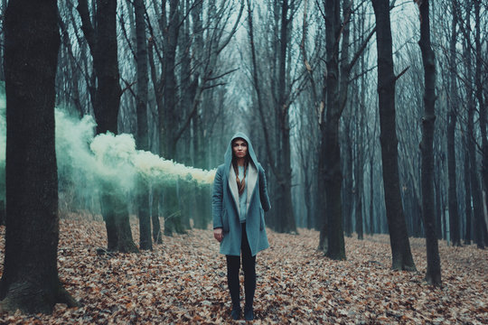 Woman holds up yellow smoke flare to signal for help in the middle of nature