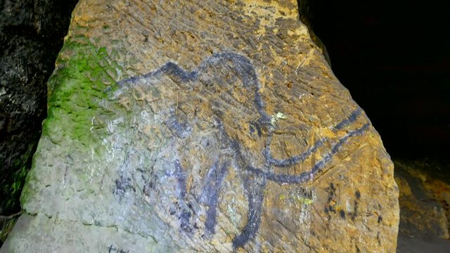 Prehistoric art of mammoth in sandstone cave. Spotlight shines on historical painting. Black carbon mammoth on sandstone wall. Paint of human hunting, prehistoric picture. Discovery of human history 