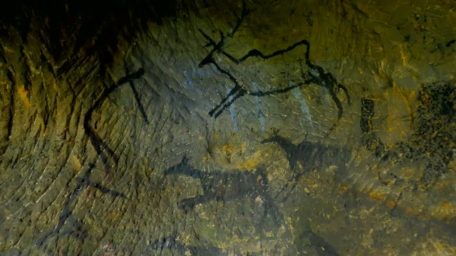 Discovery of prehistoric paint of caveman hunt in sandstone cave. Paint of human hunting of deers, mammoth and reindeer. Spotlight shines on historical black carbon abstract art in sandstone cave