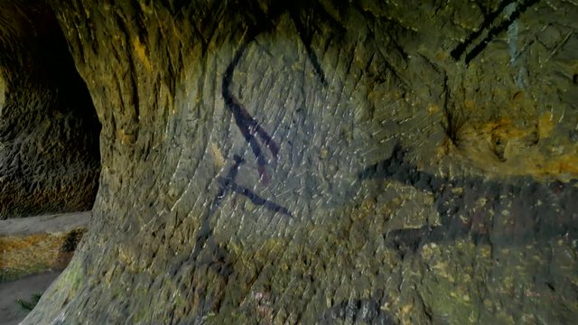 Discovery of prehistoric paint of caveman hunt in sandstone cave. Paint of human hunting of deers, mammoth and reindeer. Spotlight shines on historical black carbon abstract art in sandstone cave