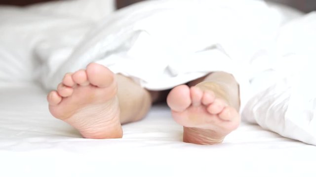 Delicate female feet moving toes playfully on white bedding