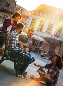 Group of  people hangout at the city street.They sitting on bench ,singing and playing guitar.