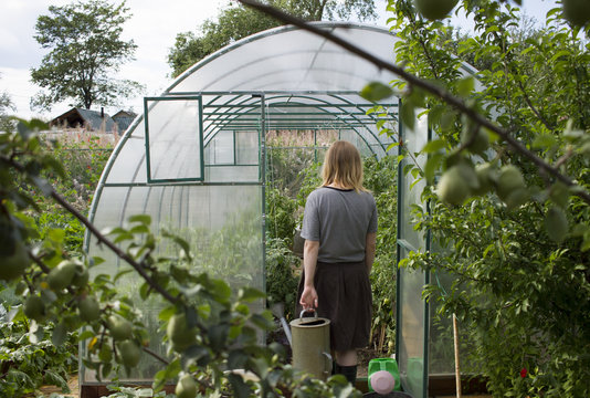 Caucasian woman carrying watering can to greenhouse