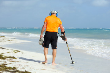 A man is walking on the beach with metal detector to find jewellery and coins.