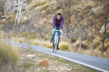 Obraz premium Cyclist man riding fixed gear sport bike in sunny day on a mountain road