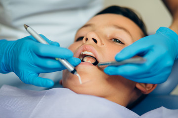 Male dentist examining boys teeth in the dentists chair. Close up picture.