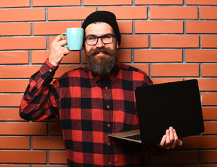 Bearded brutal caucasian hipster holding laptop with cup