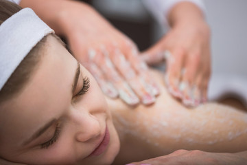 Obraz na płótnie Canvas Young smiling woman getting firming sugar scrub therapy on her back