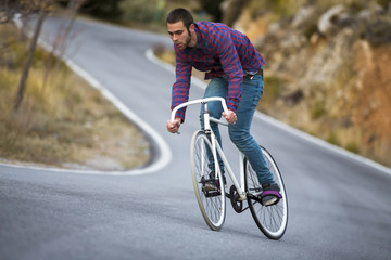 Cyclist man riding fixed gear sport bike in sunny day on a mountain road