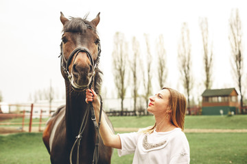 Obraz premium Beautiful girl communicates with the horse in the park. Preparing for the riding