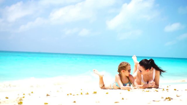 Little adorable girl and young mother at tropical beach lying on white beach and enjoy their summer vacation