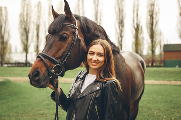 Beautiful girl communicates with the horse in the park. Preparing for the riding