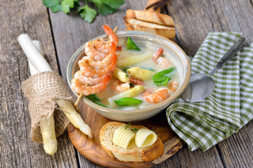 Spargelcremesuppe mit Garnelen und Zuckerschoten, mit getoastetem Butterbaguette rustikal serviert - Cream of asparagus soup with fried prawns and snow peas