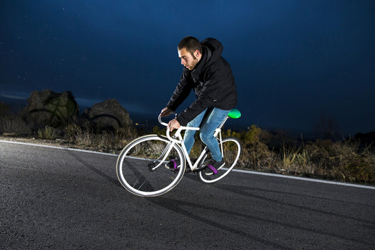 Cyclist man riding fixed gear sport bike in sunny day on a mountain road. Nocturne image.