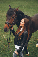 Obraz premium Beautiful girl communicates with the horse in the park. Preparing for the riding