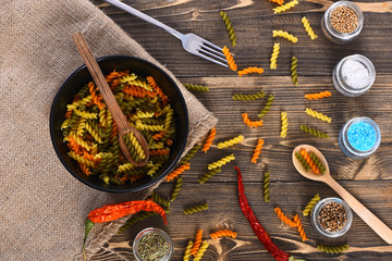 Colorful dried fusilli pasta in black bowl on sackcloth