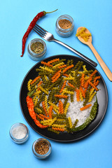 Colorful dried fusilli pasta with salt crystals on black plate