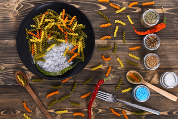 Colorful dried fusilli pasta and salt crystals in black bowl