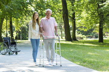 Senior man with walking frame accompanied by caregiver
