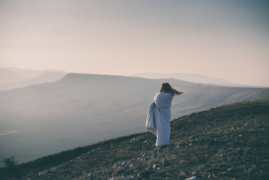 Lonely Sad And Crying Young Woman Sitting Wrapped In Blanket On Cliff Of Mountain. Toned Image