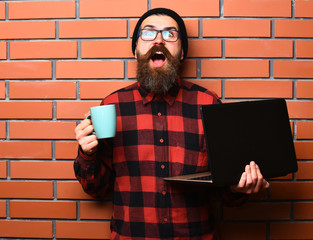 Bearded brutal caucasian hipster holding laptop with cup